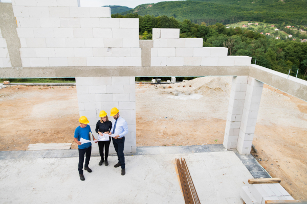 Architect, civil engineer and worker looking at plans and blueprints, discussing issues at the construction site. Aerial view.