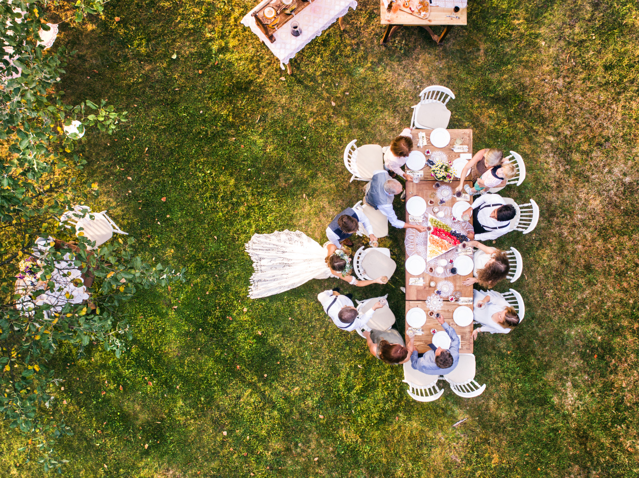 Wedding reception outside in the backyard. Bride and groom with a family standing around the table. Aerial view.