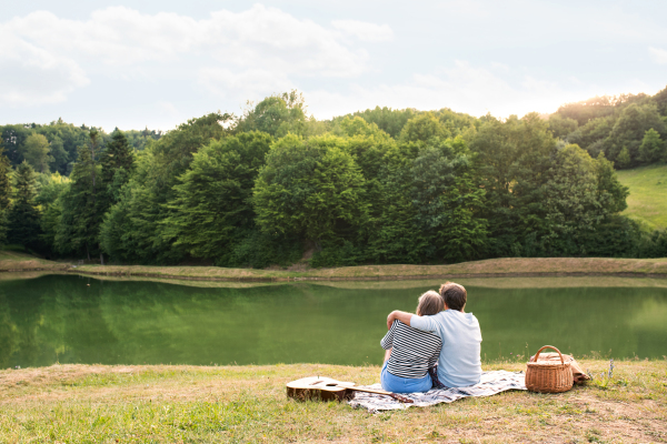 Beautiful senior couple at the lake having a picnic. Green sunny summer nature.