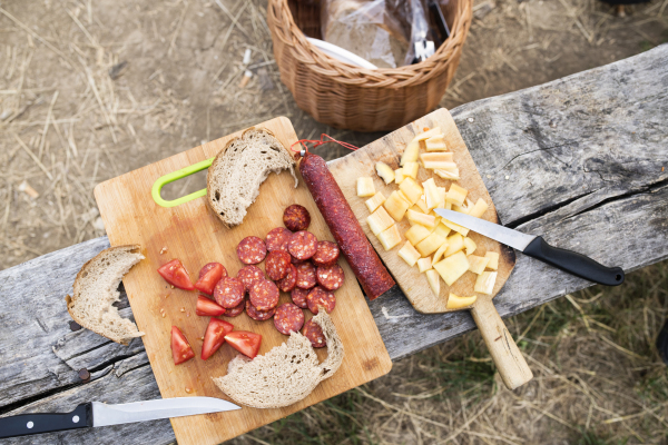 Camping in forest. Sausages, cheese, bread and vegetables on chopping board. Close up.