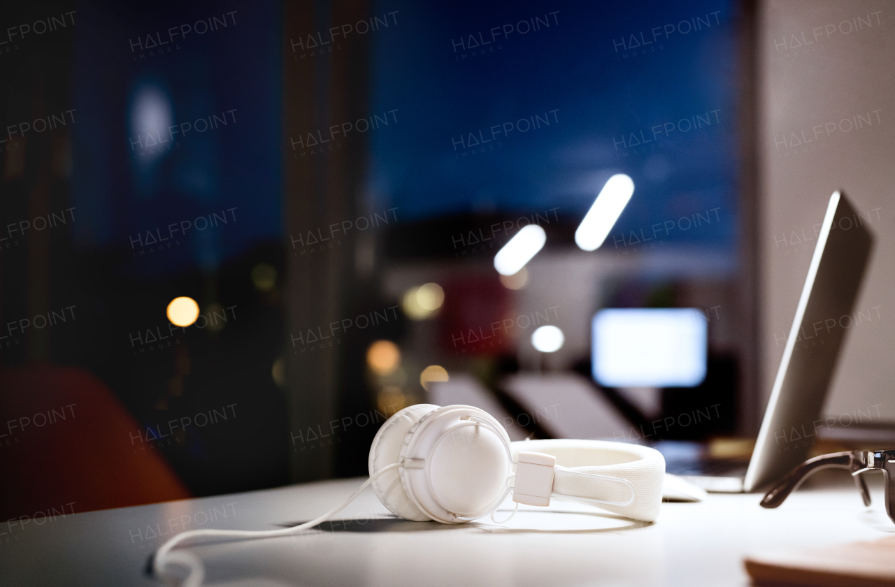 Office desk at night with computer and white earphones.