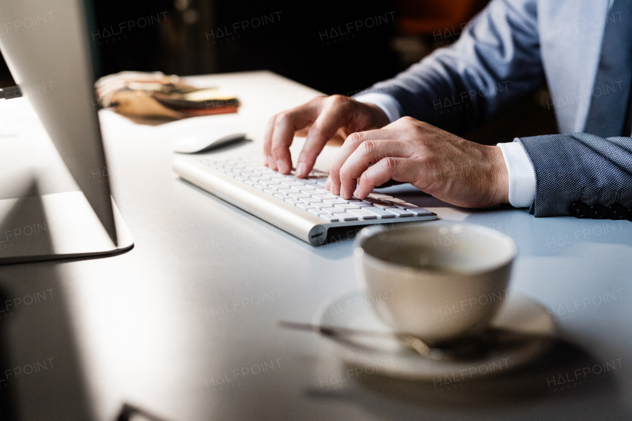 Close up of hands of unrecognizable businessman on computer keyboard in his office late at night.