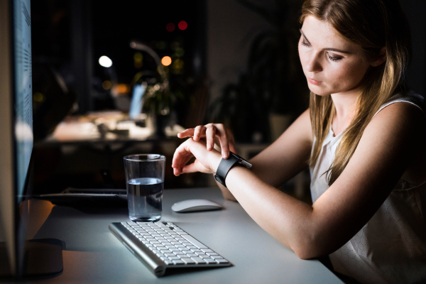 Beautiful young businesswoman in her office late at night looking at watch.