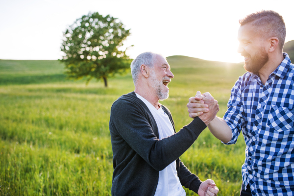 An adult hipster son with his senior father on a walk in nature at sunset.