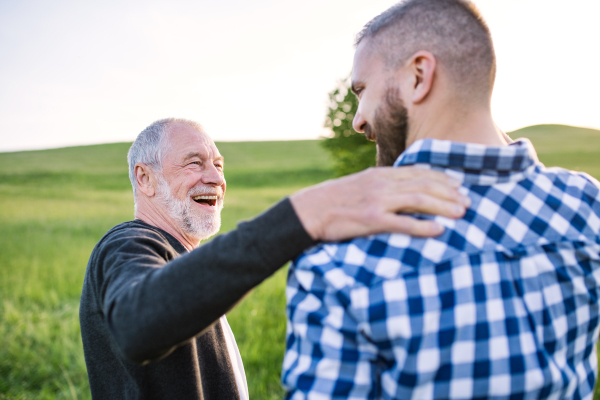 An adult hipster son with his senior father on a walk in nature at sunset, talking. Close up.