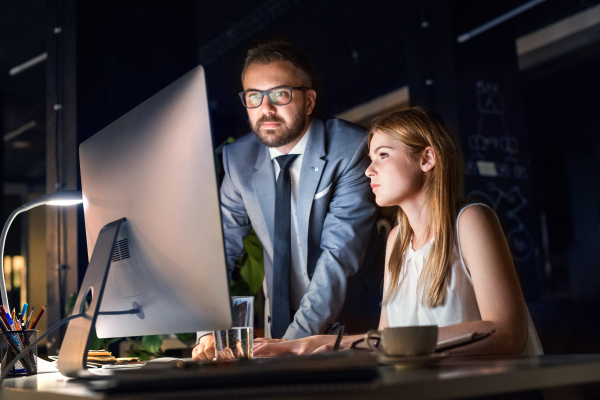 Two young businesspeople in the office at night working late, discussing a project.