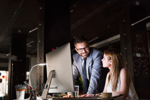 Two young businesspeople in the office at night working late, discussing a project.