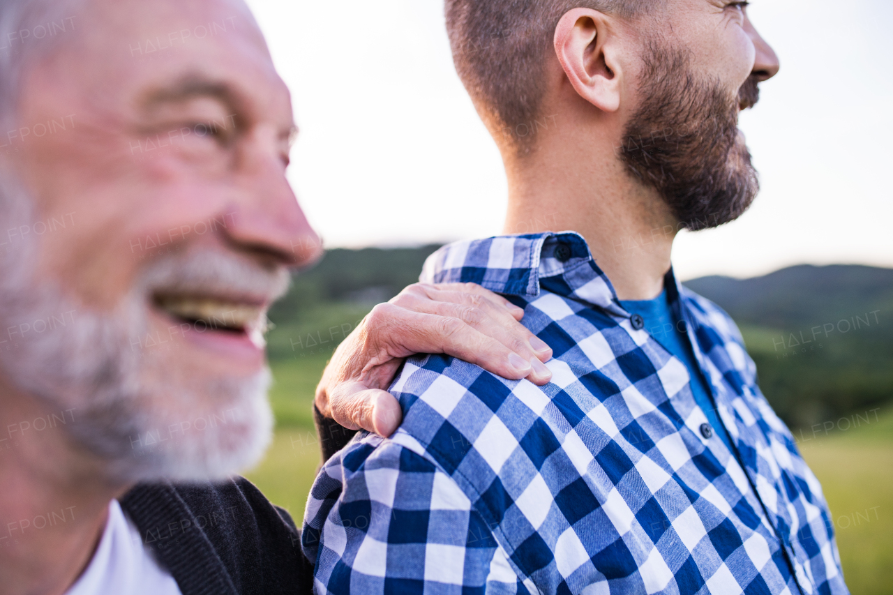 An adult hipster son with his senior father on a walk in nature at sunset. Close up.