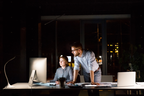 Two young businesspeople in the office at night working late, discussing a project.