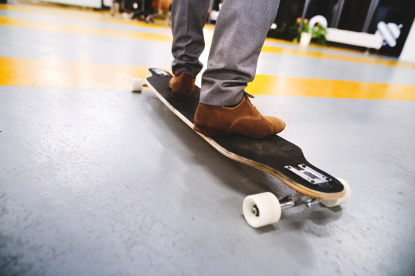 Businesspeople in the office at night working late. Unrecognizable businessman standing on longboard.