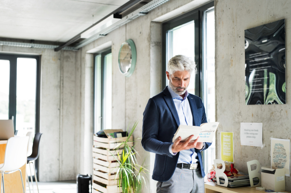 Handsome businessman in creative office reading a book.