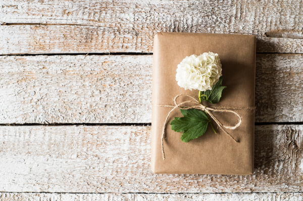 Present wrapped in brown paper decorated by lilac flower. Studio shot on white wooden background. Copy space.