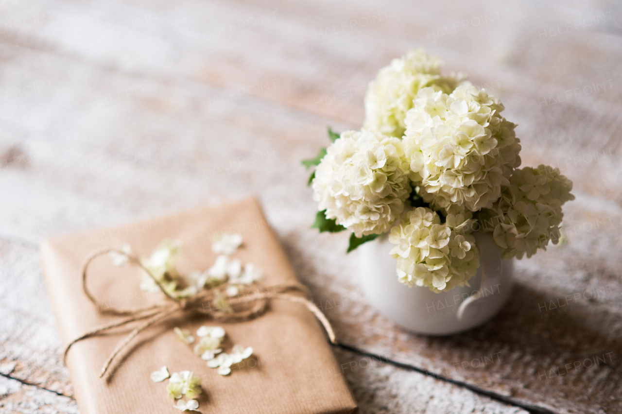 Beautiful lilac bouquet in vase laid on table and present wrapped in brown paper. Studio shot on white wooden background.