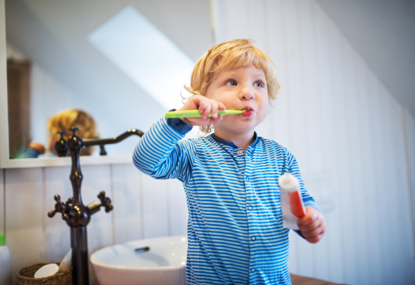 Cute toddler brushing his teeth in the bathroom. Little boy standing on a stool.