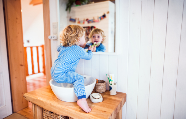 Cute toddler brushing his teeth in the bathroom. Little boy sitting on a sink. Domestic accident. Dangerous situation.