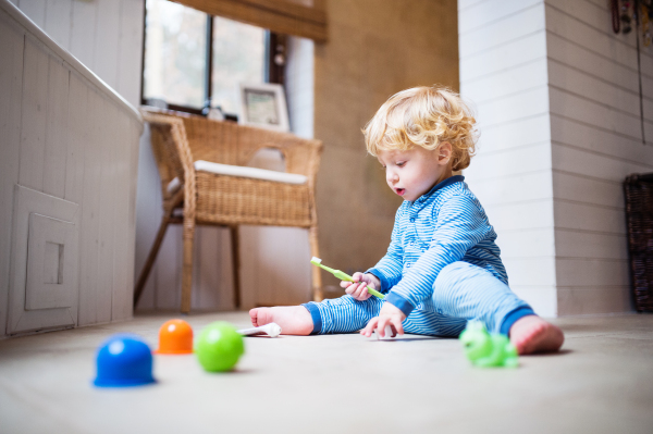 Cute toddler boy with toothbrush sitting on the floor in the bathroom.