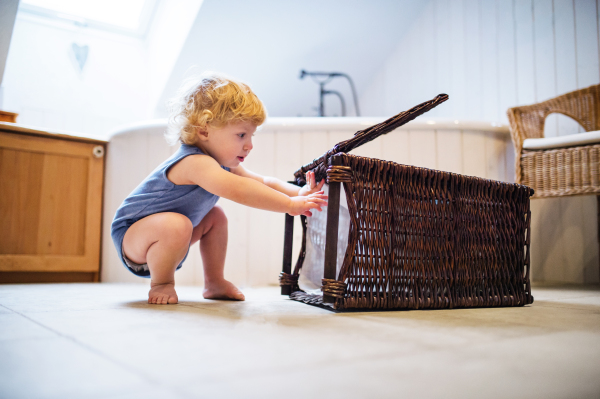 Toddler boy playing with a laundry basket in the bathroom.