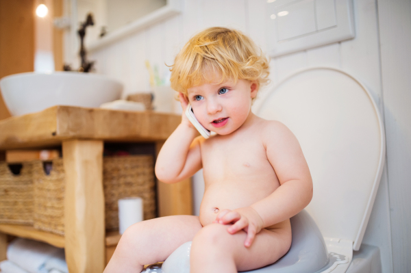 Cute toddler with a smartphone in the bathroom. Little boy sitting on the toilet.