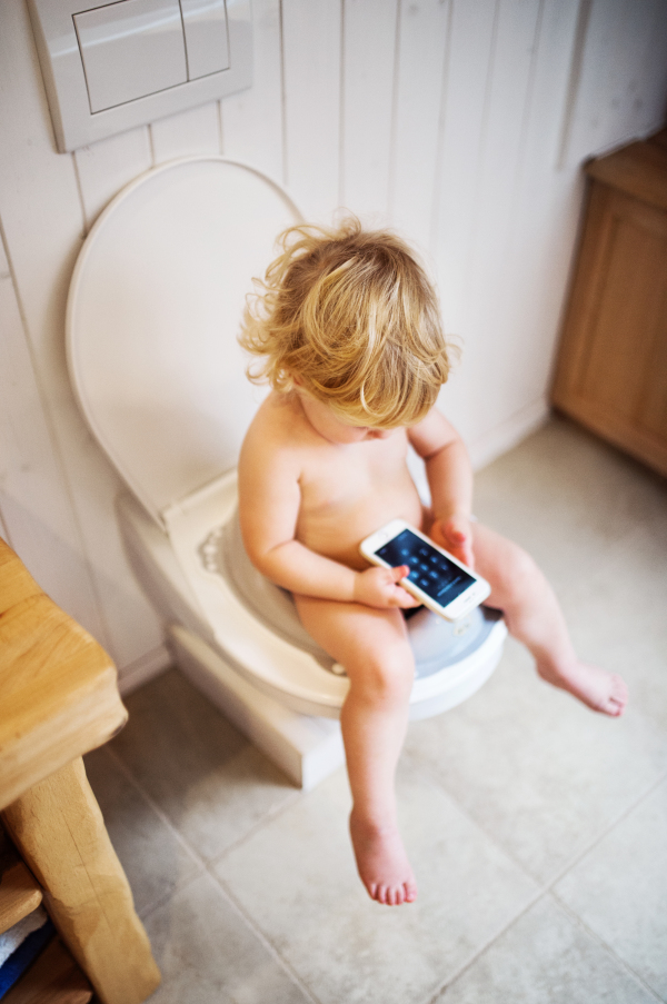 Cute toddler with a smartphone in the bathroom. Little boy sitting on the toilet.