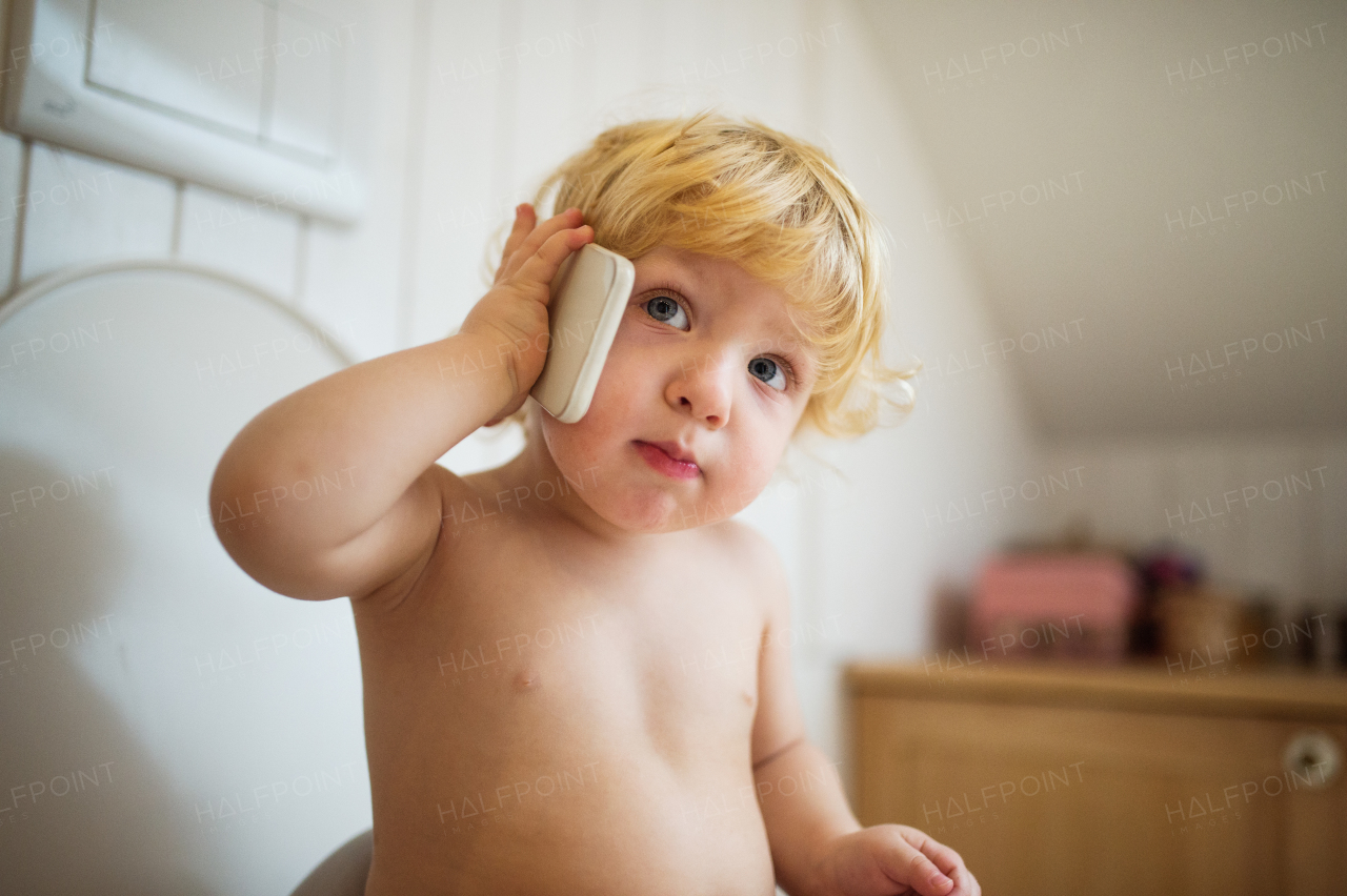 Cute toddler with a smartphone in the bathroom. Little boy sitting on the toilet.