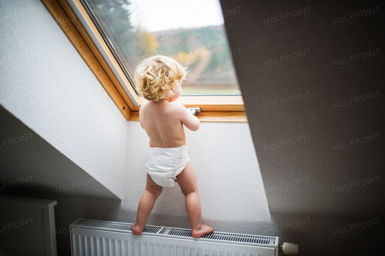 Little toddler boy standing on a radiator, opening a window. Domestic accident. Dangerous situation at home. Rear view.