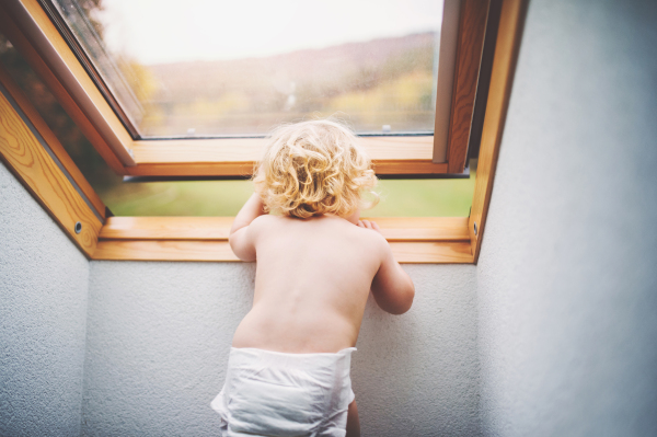 Little toddler boy opening a window. Domestic accident. Dangerous situation at home. Rear view.