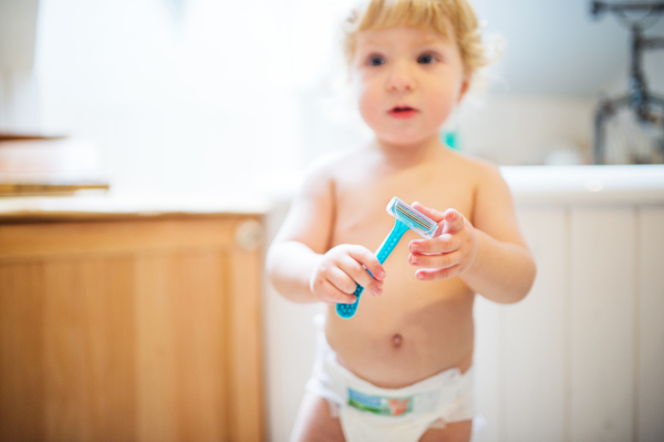 Little toddler boy holding a disposable razor. Dangerous situation at home. Domestic accident. Child safety concept.