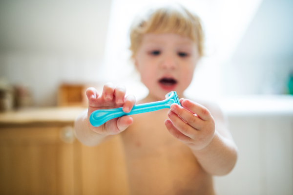 Little toddler boy holding a disposable razor. Dangerous situation at home. Domestic accident. Child safety concept.