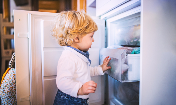 Little toddler boy opening a freezer. Domestic accident. Dangerous situation at home. Child safety concept.