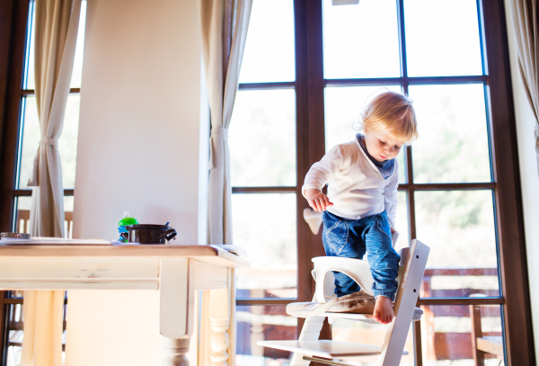 Unrecognizable little toddler boy climbing into wooden highchair at home. Domestic accident. Dangerous situation at home.