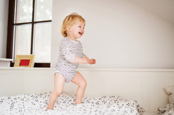 Cute toddler boy jumping on the bed in the bedroom.