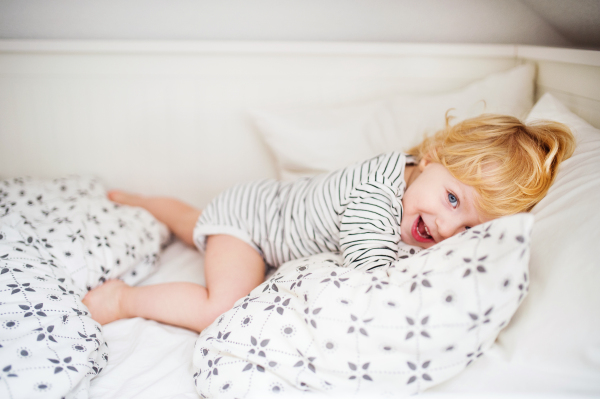 Cute happy toddler boy lying on bed at home.