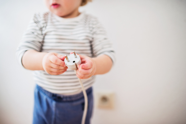 Unrecognizable little toddler playing with a plug. Domestic accident. Dangerous situation at home.