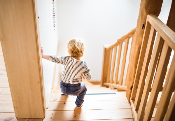 Little toddler walking down the stairs. Domestic accident. Dangerous situation at home. Child safety concept. Rear view.