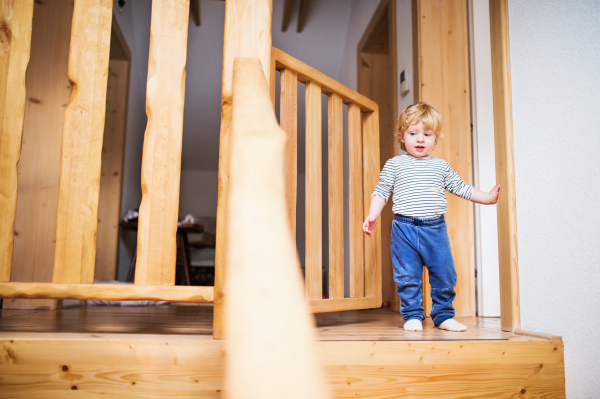 Little toddler boy standing on the top of the stairs. Domestic accident. Dangerous situation at home. Child safety concept.