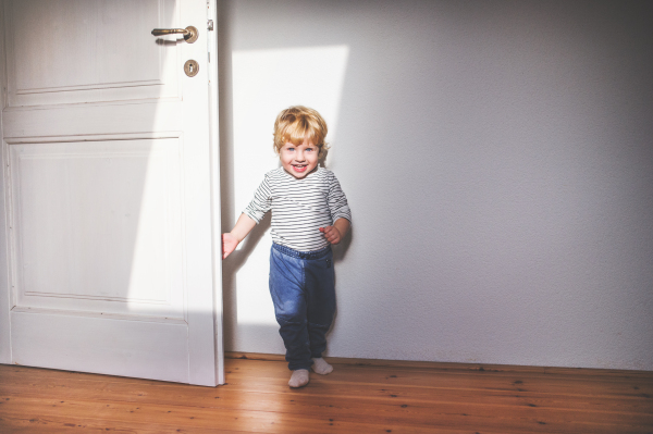 Cute happy toddler boy standing in a bedroom.