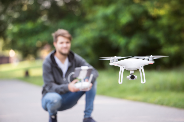 Young hipster man with remote control and flying drone with camera. Green sunny nature.