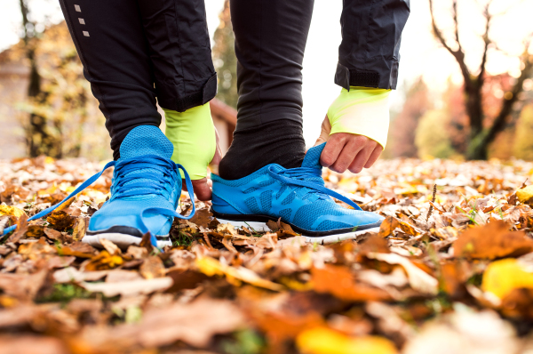 Unrecognizable young runner putting on sports shoes. Autumn nature.