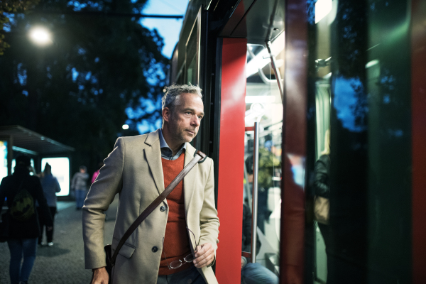 Mature businessman with suitcase getting on a tram or a trolley car in the evening in Prague city.