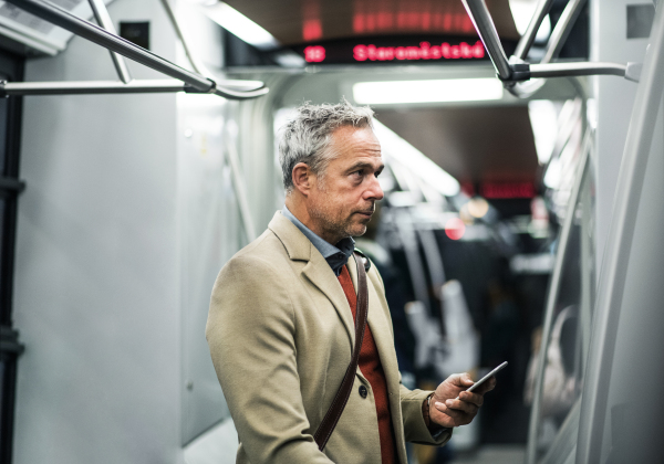 Mature handsome businessman with smartphone travelling by subway in city of Prague.