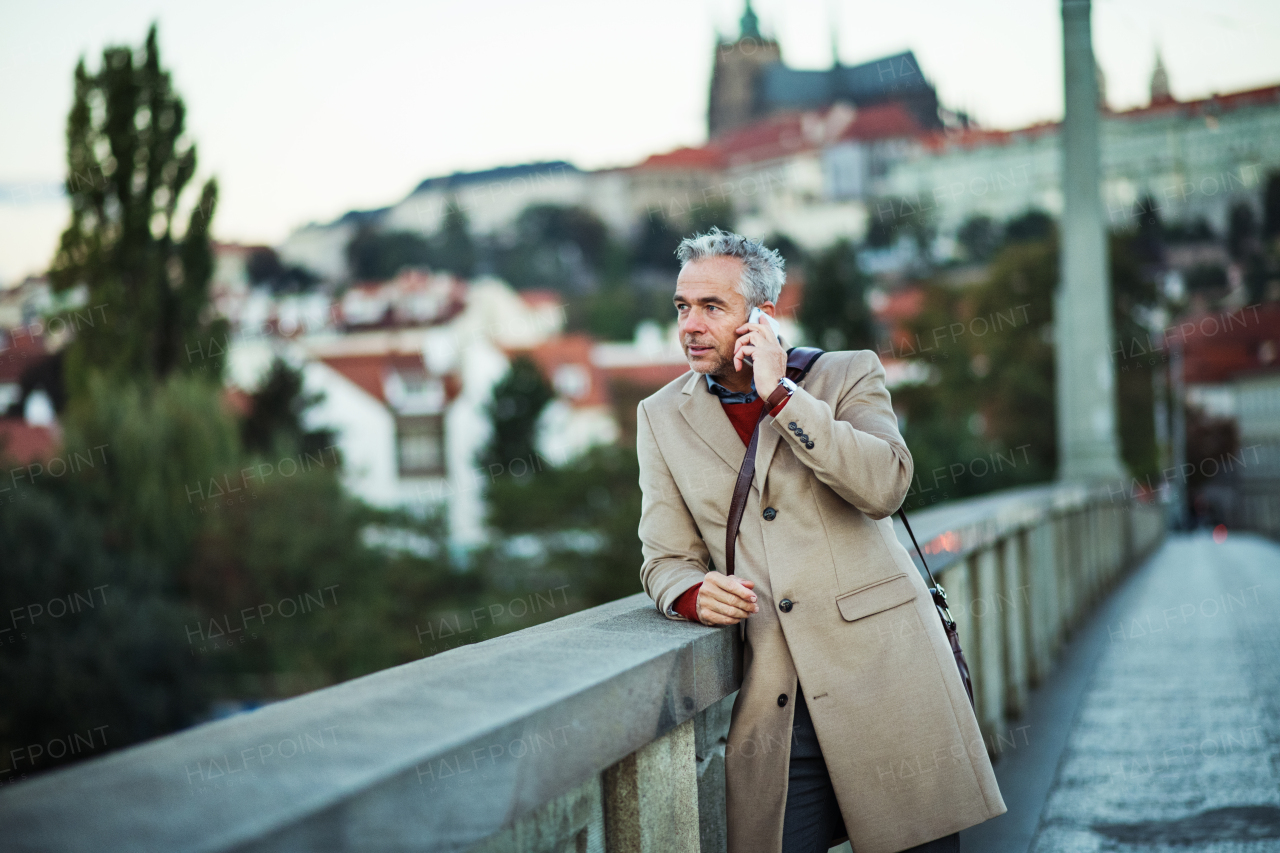 Mature businessman with smartphone standing on a bridge in city, making a phone call.