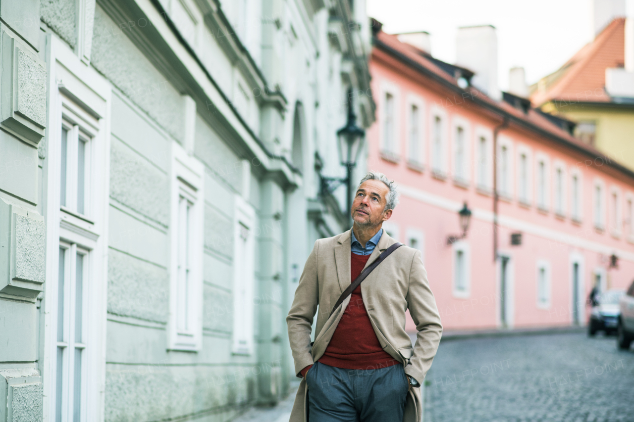 A mature businessman walking on a street in Prague city, hands in pockets. Copy space.