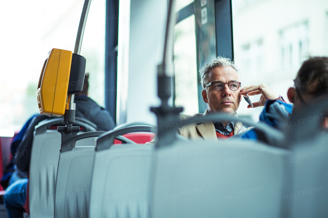 Mature handsome businessman with smartphone travellling by bus in city, making phone call. Copy space.