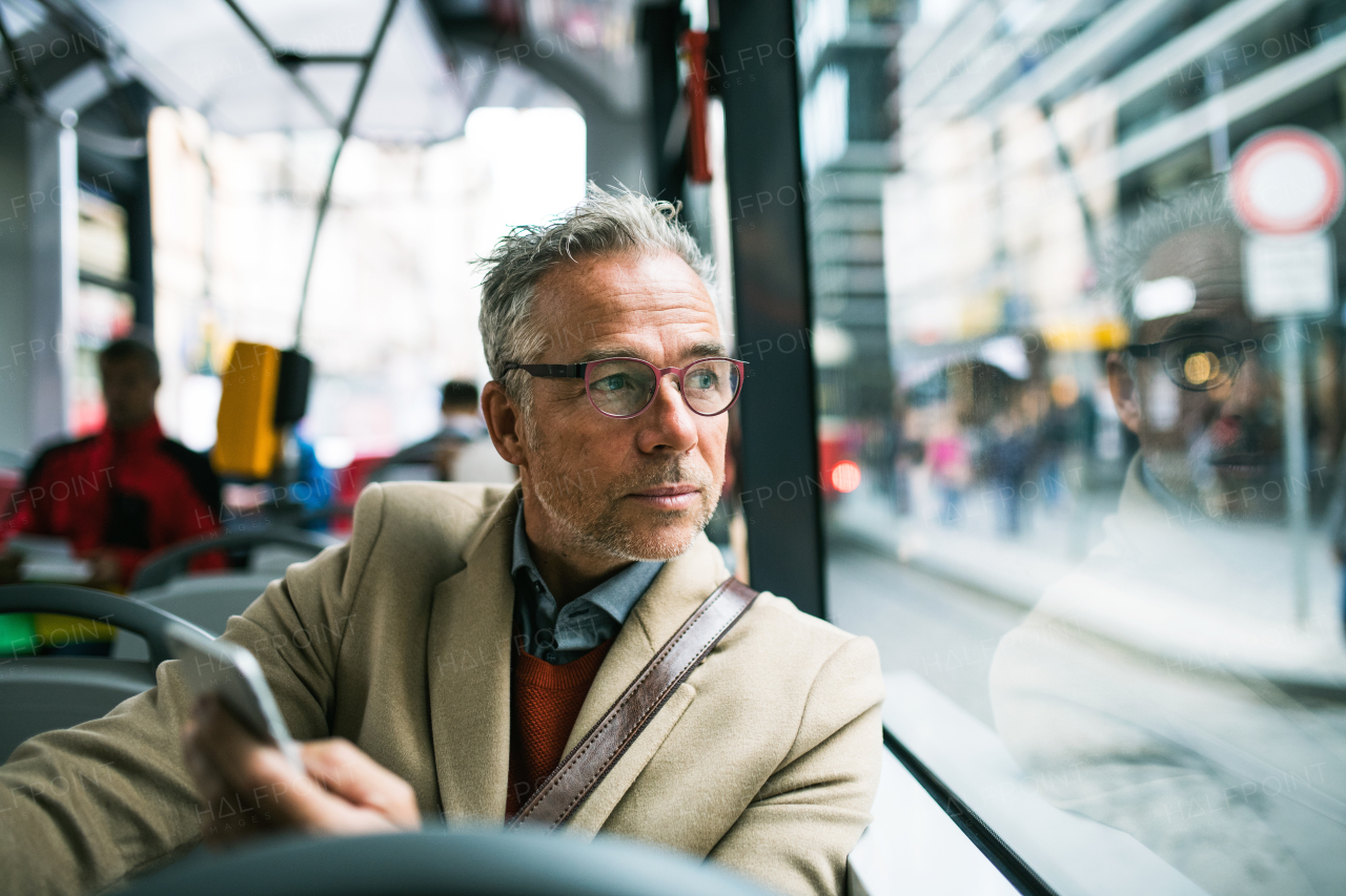 Mature handsome businessman with smartphone travellling by bus in city of Prague. Copy space.