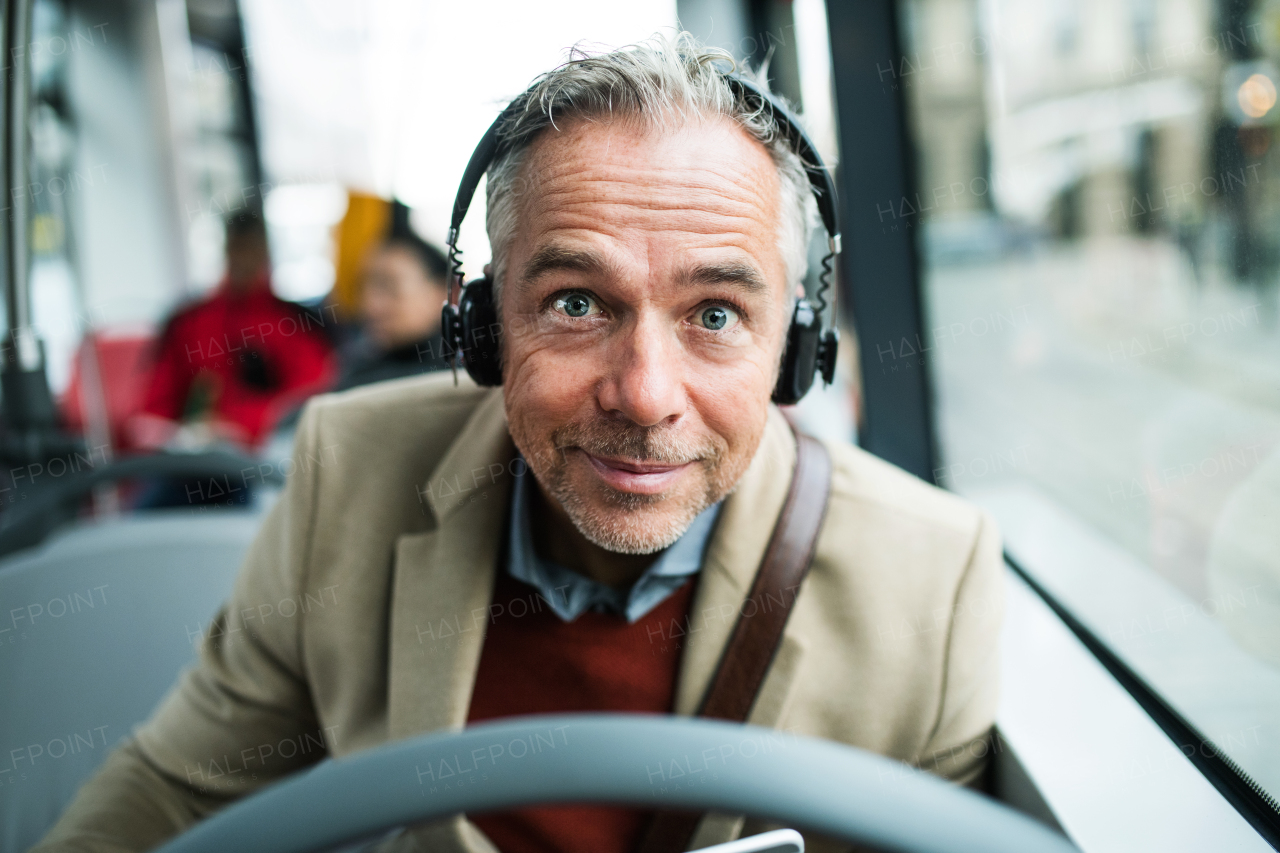 Mature tired businessman with heaphones travellling by bus in city, listening to music.