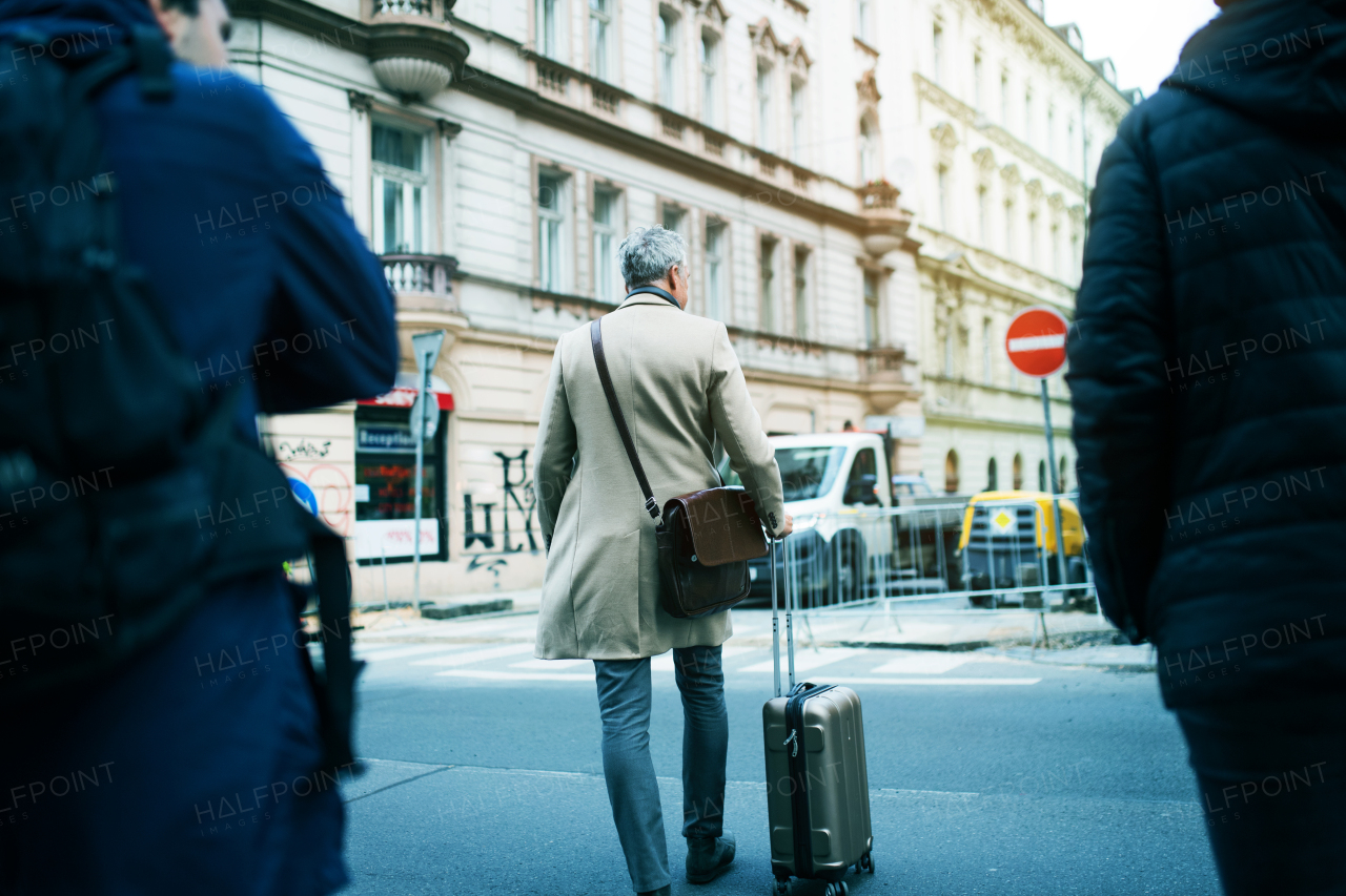 A rear view of mature businessman with suitcase walking on a street in Prague city.