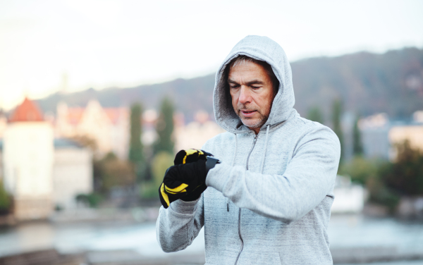 Mature male runner with water bottle standing outdoors in city, checking the time when resting after the run.