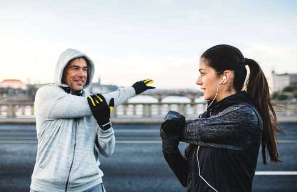 A fit sporty couple runners doing stretching outdoors on the bridge in Prague city, Czech Republic.