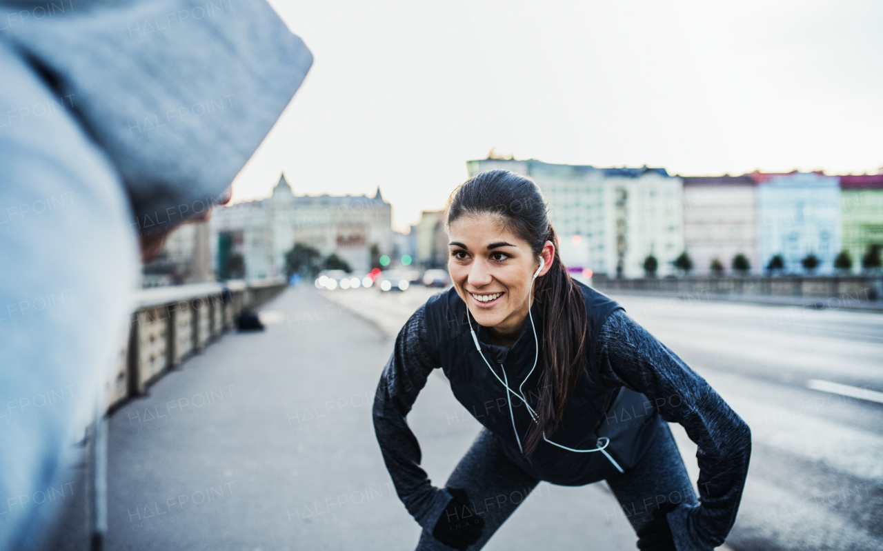 A fit sporty couple with earphones runners stretching outdoors on the streets of Prague city.