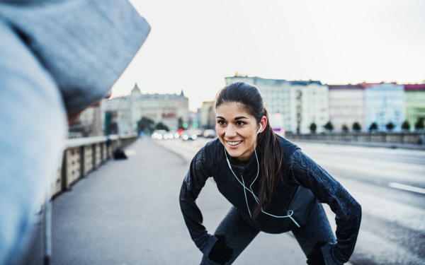 A fit sporty couple with earphones runners stretching outdoors on the streets of Prague city.